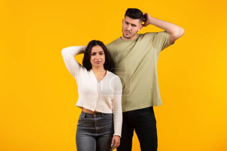 Foto de Thoughtful sad young arab couple in casual thinking, scratching head with hands, isolated on yellow background, studio. Question, choice, relationship problems, creating idea, what to do emotions - Imagen libre de derechos