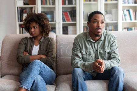 Foto de Sad unhappy young black man and woman in casual sitting on couch at home, feeling down after quarrel, african american spouses having fight, experiencing difficulties in marriage, relationships - Imagen libre de derechos