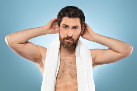 Foto de Handsome middle aged caucasian man looking at camera, putting wax, touching his hair, styling or checking for hair loss problem, posing with towel on neck over blue background - Imagen libre de derechos