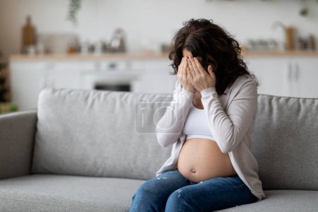 Téléchargez les photos : Portrait Of Young Pregnant Woman Crying While Sitting On Couch At Home, Upset Expectant Lady Covering Face With Hands, Suffering Hormonal Changes During Pregnancy Or Depression, Copy Space - en image libre de droit