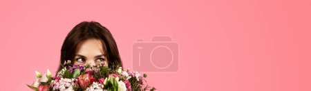 Foto de Smiling young caucasian lady enjoy aroma of bouquet of flowers, rejoices at gift, isolated on pink background, panorama, studio. Celebration of birthday, holiday in spring, lifestyle, ad and offer - Imagen libre de derechos