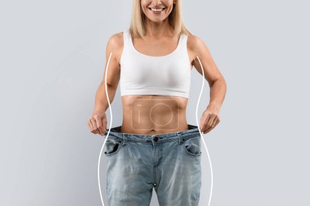 Photo for Unrecognizable woman wearing white top and oversize jeans, showing amazing results of healthy diet or detox, figure shape lines on both sides of lady, weight loss concept, cropped studio shot, collage - Royalty Free Image