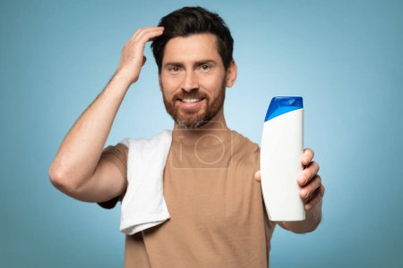 Téléchargez les photos : My choice. Handsome bearded man having stylish haircut, ready to take shower, standing with towel on shoulder, focus on bottle. Daily morning routine - en image libre de droit
