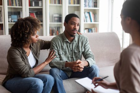 Foto de Loving attractive young black woman embracing her depressed frustrated husband looking at copy space, african american couple have therapy session with family psychologist. Marital crisis concept - Imagen libre de derechos