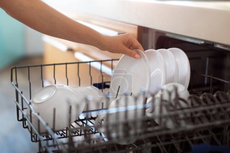 Foto de Unrecognizable Woman Unloading Clean Dishes From Dishwasher Machine In Kitchen, Female Hand Taking Out Plate After Cleaning, Enjoying Making Domestic Chores At Home, Closeup Shot, Cropped - Imagen libre de derechos