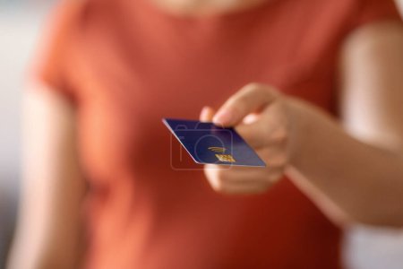 Unrecognizable woman holding bank credit card and giving it at camera, closeup shot of young female making cashless payment while doing shopping, paying for purchases, cropped image