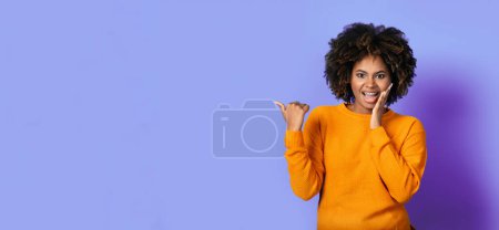 Amazed beautiful stylish bright african american young woman with teeth braces showing empty space over purple studio background, pointing at exciting deal and grimacing, web-banner