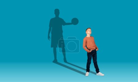 Téléchargez les photos : Childhood and dream about big and famous future. Conceptual image with boy and drawned shadow of sportive male basketball player behind on blue background. Copy space for ad, text, collage - en image libre de droit