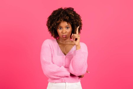 Foto de Happy pretty young black curly female in casual raising finger up at copy space, got idea, isolated on pink background, studio. Facial expression, great solution, brainstorm, advice, ad and offer - Imagen libre de derechos