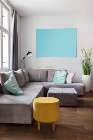 Photo for Stylish Interior Of Cozy Living Room With Big Grey Sofa And Yellow Pouf Chair, Closeup Indoor Shot Of Room In Modern Apartment With Blue Empty Poster On Wall And Panoramic Window, Copy Space - Royalty Free Image