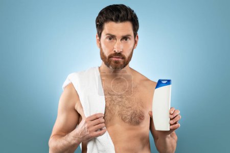 Foto de Handsome caucasian man holding shampoo bottle, advertising male cosmetic product, standing on blue background, studio shot, mockup - Imagen libre de derechos