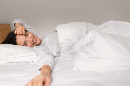 Téléchargez les photos : Jeune femme européenne souriante dormant sur un lit blanc, se réveillant, appréciant le bon matin, le week-end ou le temps libre, vacances à l'intérieur de la chambre. Repos et détente à la maison, soins de santé, paresseux et mode de vie - en image libre de droit