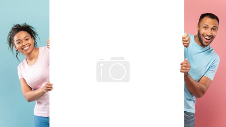 Téléchargez les photos : Panneau publicitaire de promotion. Homme noir excité et dame tenant tableau publicitaire blanc, debout sur fond rose et bleu coupé en deux, panorama avec espace libre de copie - en image libre de droit