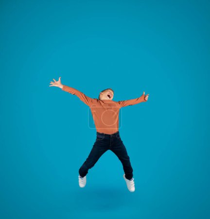 Téléchargez les photos : Overjoyed Little Boy Jumping In Air Over Blue Studio Background, Positive Carefree Preteen Male Child Having Fun, Emotionally Reacting To Win Or Good News, Full Length Shot With Copy Space - en image libre de droit