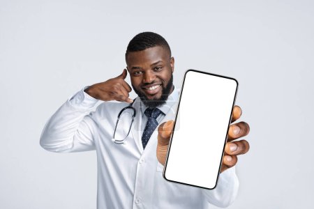 Téléchargez les photos : Cheerful Black Male Doctor Showing Big Blank Smartphone And Gesturing Call Me, Smiling African American Physician Man In Uniform Demonstrating Empty Cellphone With Copy Space, Collage, Mockup - en image libre de droit