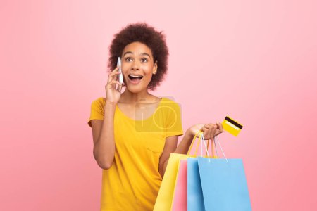 Téléchargez les photos : Cheerful excited shocked millennial multiethnic lady in casual with open mouth calling by phone, hold many shopping bags isolated on pink background, studio. Sale, shopping, gossip, great ad and offer - en image libre de droit