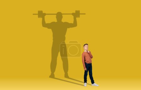 Téléchargez les photos : Childhood and dream about big and famous future. Conceptual image with kid and drawned shadow of sportive athletic male bodybuilder behind on yellow background. Copy space for ad, text, collage - en image libre de droit