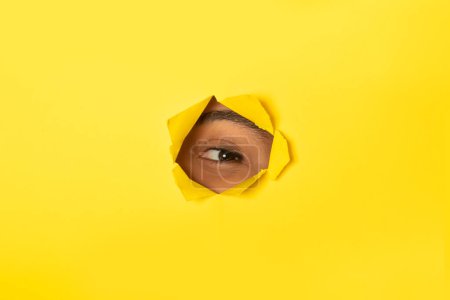 Foto de Interesado dama negra mirando a través del agujero en papel amarillo roto, mujer mirando a la cámara, primer plano, espacio libre. Te estoy observando, concepto de curiosidad - Imagen libre de derechos