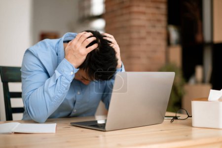 Photo for Work problems. Male entrepreneur siting at desk and touching head in despair while working on laptop at home office, free space. Depressed businessman got bad news - Royalty Free Image