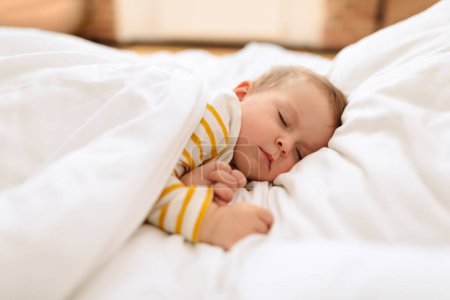 Foto de Baby girl sleeping on side, lying under the blanket on white bedding, closeup, free space. Cute toddler child napping during daytime sleep at home - Imagen libre de derechos