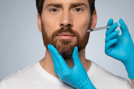 Téléchargez les photos : Middle aged man getting anti-aging procedure at clinic or salon, cosmetician hands in gloves making beauty injection for handsome man over grey studio background - en image libre de droit