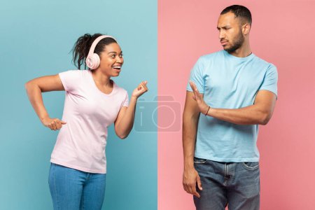 Téléchargez les photos : Joyeuse femme noire dansant dans un casque sans fil, se sentant heureuse, un homme sérieux faisant un geste d'arrêt, demandant de se calmer, debout sur un fond bleu et rose coupé en deux - en image libre de droit