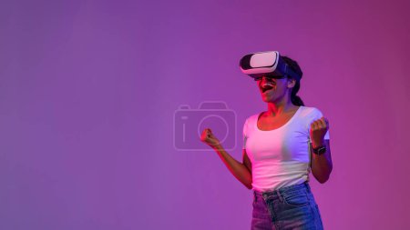 Photo for Portrait Of Excited Young Black Woman In VR Glasses Celebrating Success, Emotional African American Lady Cheering Online Win While Standing Under Neon Lighting Over Purple Background, Panorama - Royalty Free Image