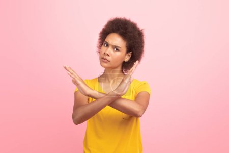 Foto de Strict angry millennial multiethnic woman in casual making stop sign with crossed arms isolated on pink background, studio. Fight against harassment, discrimination, end gesture, power and lifestyle - Imagen libre de derechos
