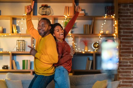 Photo for Crazy black couple recording video content, dancing on smartphone camera at home. Positive african boyfriend and girlfriend filming for social media, using mobile device. Blogging, blogger concept - Royalty Free Image