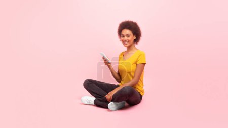 Photo for Cheerful millennial multiethnic woman in casual typing on smartphone, chatting, watch video, surfing internet isolated on pink background, studio. App for study, work in social networks, ad and offer - Royalty Free Image