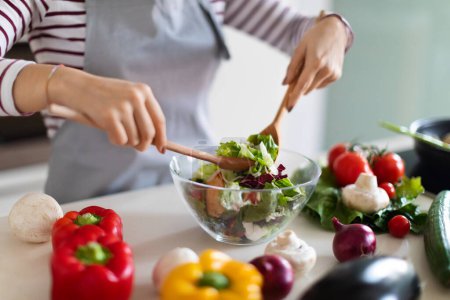 Photo for Cooking concept. Unrecognizable woman in grey apron chef making fresh organic vegetable salad, cropped of lady preparing delicious healthy meal at home, mixing veggies in bowl, closeup, copy space - Royalty Free Image
