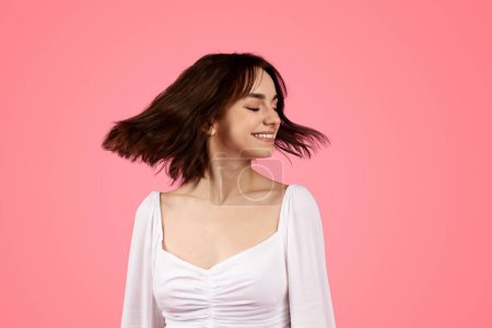 Téléchargez les photos : Cheerful pretty young european female turn head with closed eyes, enjoy freedom, lifestyle and holiday, isolated on pink background, studio. Fun alone, spare time, celebration huge sale, ad and offer - en image libre de droit