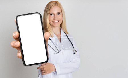 Photo for Female Doctor With Stethoscope Showing Big Blank Smartphone At Camera, Smiling Therapist Woman Wearing Uniform Recommending New Mobile App For Online Medical Services, Collage, Mockup - Royalty Free Image