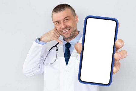 Photo for Smiling middle aged male doctor showing blank smartphone and making call me gesture, professional medical worker in uniform demonstrating empty mobile phone with white screen, collage, mockup - Royalty Free Image