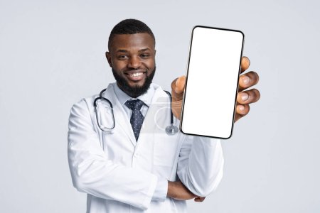 Photo for Medical Offer. Black Male Doctor In Uniform Demonstrating Smartphone With Blank Screen At Camera, Smiling African American Physician Man Holding Empty Cellphone In Hand, Collage, Mockup - Royalty Free Image