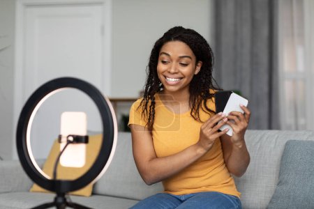 Téléchargez les photos : Happy African American femelle vlogger enregistrement vidéo examen de nouveaux smartphones, montrant appareil électronique à la caméra de téléphone portable, la promotion du nouveau modèle de gadget - en image libre de droit