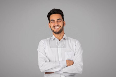 Photo for Smiling Handsome Young Arab Businessman With Folded Arms Standing Over Grey Background And Looking At Camera, Happy Middle Eastern Male Entrepreneur In White Shirt Posing In Studio, Copy Space - Royalty Free Image