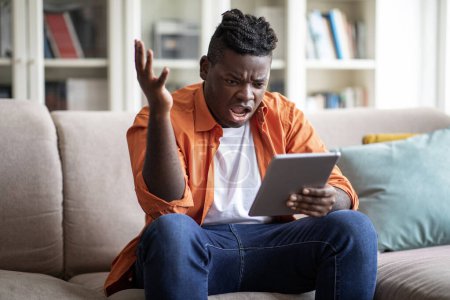 Photo for Angry african american young man gesturing and yelling, receive bad unexpected message on digital tablet, chubby black guy furious with problems with business, reading news online at home - Royalty Free Image