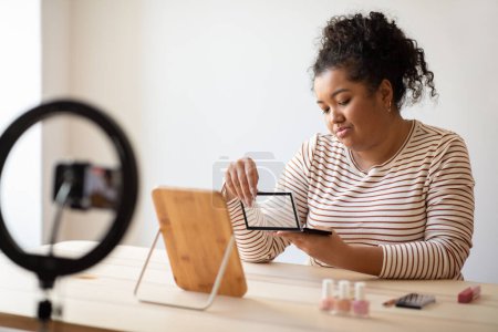 Téléchargez les photos : Disappointed beauty influencer curly hispanic overweight young lady sitting at vanity table at home, reviewing eyeshadow palette, streaming from home, using blogger set, dont recommend beauty product - en image libre de droit