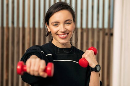 Photo for Smiling caucasian millennial lady in sportswear doing exercises with dumbbells for hands on street, enjoy weight loss, close up. Sports, fitness, workout and active in city, body and health care - Royalty Free Image