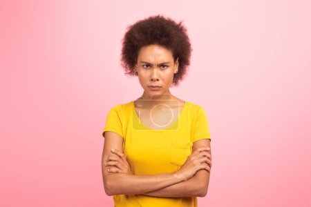 Foto de Sad strict angry young black curly female crossed her arms on chest and looks at camera, isolated on pink background, studio. Human emotions, problems, resentment, fight against violence, harassment - Imagen libre de derechos