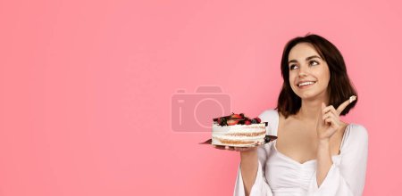 Photo for Thoughtful happy young european woman hold cake, thinking, looking at empty space, isolated on pink background, studio, panorama. Celebration holiday, birthday, dreams, make a wish, ad and offer - Royalty Free Image