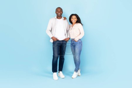 Téléchargez les photos : Full length portrait of happy black couple smiling at camera and posing, standing over blue studio wall, cheerful lady leaning on her husbands shoulder, copy space - en image libre de droit