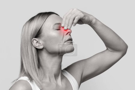 Foto de Mujer rubia de mediana edad con hemorragia nasal o epistaxis tocándose la nariz aligerada en rojo, ojos cerrados, foto en blanco y negro, fondo del estudio, primer plano - Imagen libre de derechos