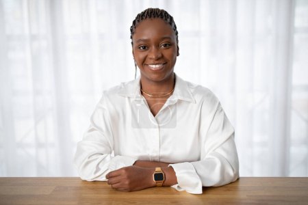 Téléchargez les photos : Positive cheerful beautiful young black businesswoman in formal outfit sitting at workdesk at office or at home, smiling at camera, copy space. Women in business concept - en image libre de droit