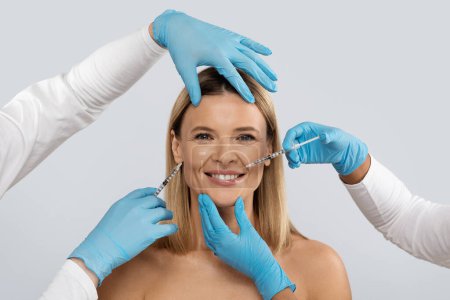 Photo for Smiling attractive blonde middle aged woman gets cosmetic injection in her face, closeup. Hyaluronic acid injection for facial rejuvenation procedure. Women in beauty salon. Plastic surgery clinic. - Royalty Free Image