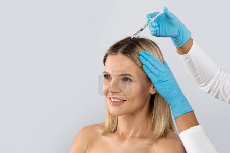 Photo for Beautician injections for healthy hair growth. Mesotherapy of the scalp. Middle aged woman undergoing course of spa treatments for healthy strong hair, isolated on studio background, copy space - Royalty Free Image