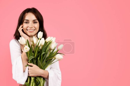 Foto de Joven mujer europea alegre con ramo de tulipanes, disfrutar de estilo de vida, regocijarse vacaciones de primavera, celebrar cumpleaños, aislado en el fondo rosa, estudio. Ternura, cuidado de belleza, regalo, anuncio y oferta - Imagen libre de derechos
