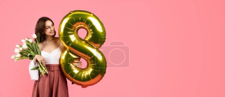 Téléchargez les photos : Happy young european female hold bouquet of flowers and balloon number 8, rejoices to holiday of spring, looks at empty space isolated on pink background, studio. Gift, congratulation, ad and offer - en image libre de droit