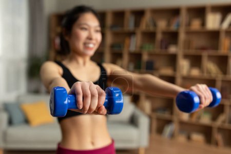Téléchargez les photos : Domestic sports. Young asian lady doing exercises with weights, working out with dumbbells at home, selective focus. Korean woman strengthening arm muscles, training in living room - en image libre de droit